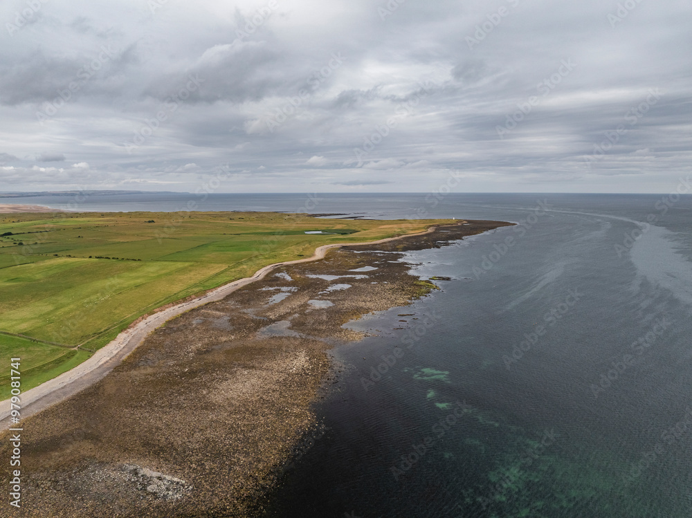 Aerial view of the rugged coastline and serene sea with picturesque fields under a cloudy sky, Holy Island, Berwick-upon-Tweed, England. Aerial view of the rugged coastline and serene sea with picturesque fields under a cloudy sky, Holy Island, Berwick-upon-Tweed, England.