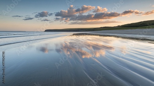 A serene beach scene with calm, shallow water reflecting the sky and clouds at sunset. The sand is wet and textured, with a distant shoreline in the background.