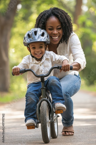 Mother teaching her son to ride a bicycle in a sunny park path, showcasing family bonding and joyful moments outdoors