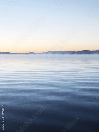 A serene and tranquil landscape with a still lake and a misty horizon at sunrise or sunset. The water is calm and reflects the soft colors of the sky.