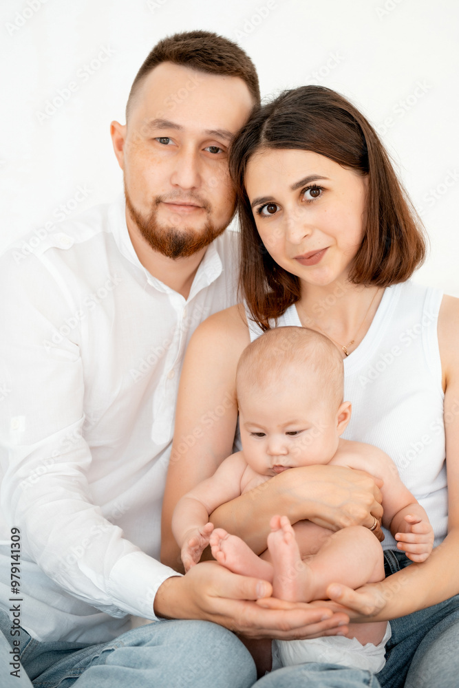 mom, dad with a baby, an international family, a Caucasian mom with an Asian husband and a baby in her arms in the bedroom gently hugs the baby holding in her arms, a place for text mom, dad with a baby, an international family, a Caucasian mom with an Asian husband and a baby in her arms in the bedroom gently hugs the baby holding in her arms, a place for text