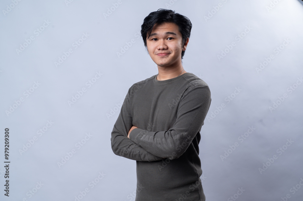 An Asian man wearing a long-sleeve gray shirt with arms crossed, giving a confident and slight smile. He is posing in front of a white background An Asian man wearing a long-sleeve gray shirt with arms crossed, giving a confident and slight smile. He is posing in front of a white background