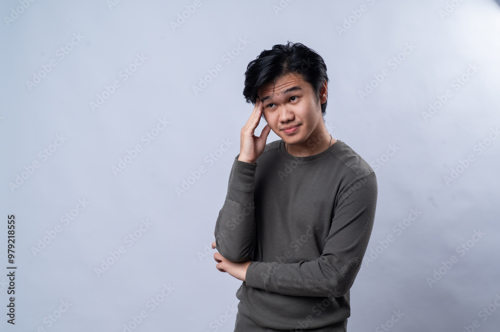 An Asian man is wearing a gray long-sleeved shirt, holding his forehead with a pained expression as if suffering from a headache. The background is white