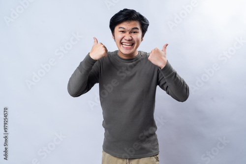 An Asian man in a casual gray long-sleeve shirt gives a thumbs-up gesture, smiling confidently. The image is shot in a studio with a plain white background, highlighting positivity and approval