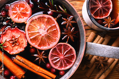 Close up of copper pot with red mulled wine with slices of orange, apple, cinnamon, star anise, rosemary and cranberries. Food photography