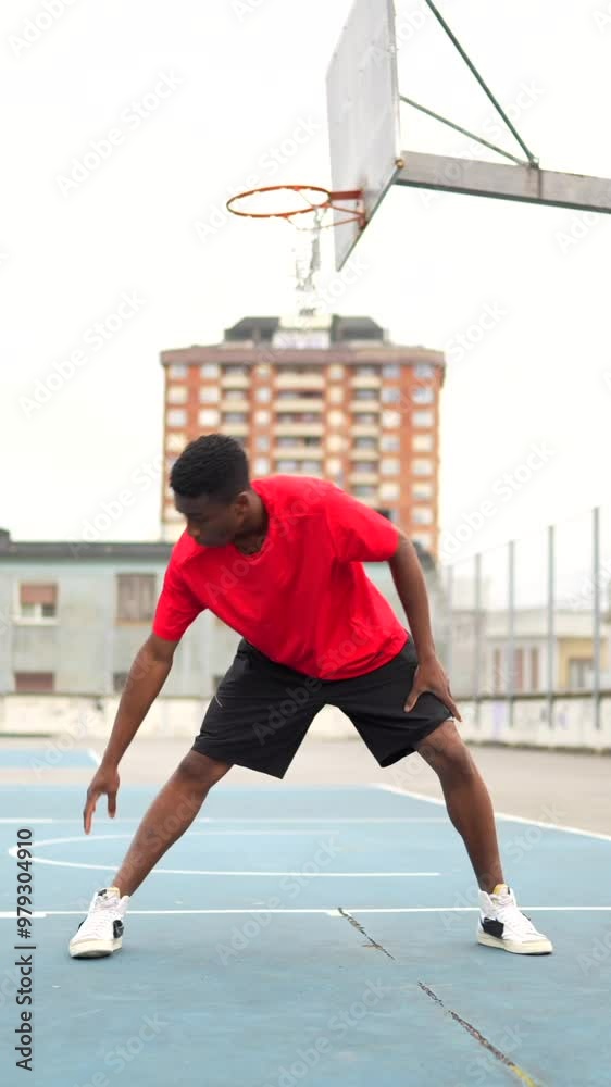 Vertical portrait of an African american basketball player resting sitting on an outdoor court Vertical portrait of an African american basketball player resting sitting on an outdoor court