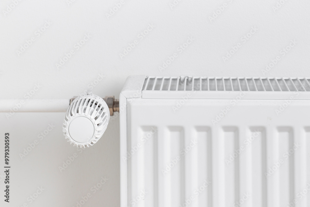 A close-up of a radiator with a temperature control dial mounted on a white wall A close-up of a radiator with a temperature control dial mounted on a white wall