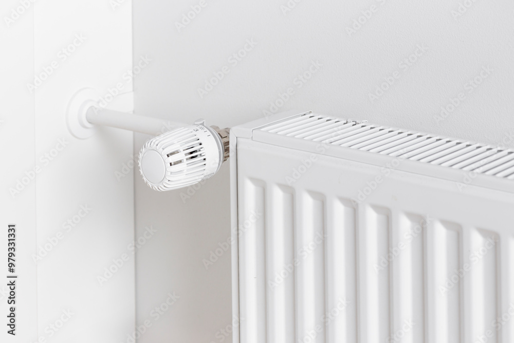 A close-up of a radiator with a temperature control dial mounted on a white wall A close-up of a radiator with a temperature control dial mounted on a white wall