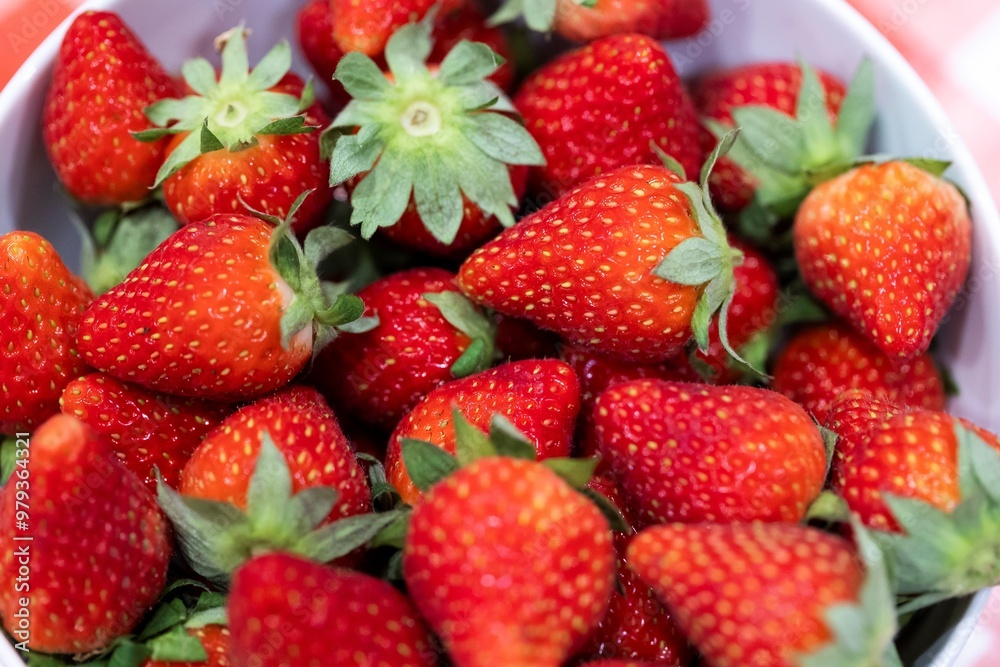 A closeup of a bunch of red delicious fresh strawberies with the green top in a white bowl. The tasty fruit is ready to be eaten. A closeup of a bunch of red delicious fresh strawberies with the green top in a white bowl. The tasty fruit is ready to be eaten.