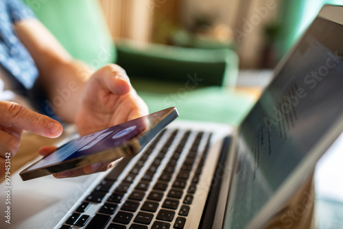 Man relaxing on green couch working from home with smartphone and laptop