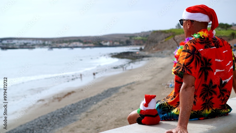 Obraz premium Tourist with Santa Claus doll enjoys tropical climate watching sunbathers in front of sea of ​​tourist resort. Christmas tropical vacation concepts