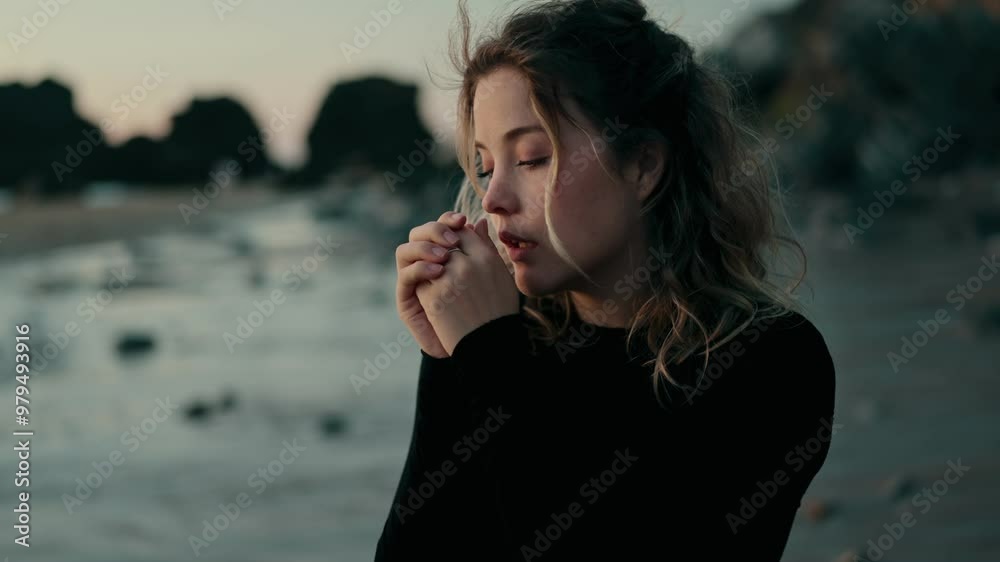 A woman stands on a chilly beach, hands clasped together as she tries to warm up. The ocean waves create a serene background, capturing a moment of solitude and reflection. A woman stands on a chilly beach, hands clasped together as she tries to warm up. The ocean waves create a serene background, capturing a moment of solitude and reflection.
