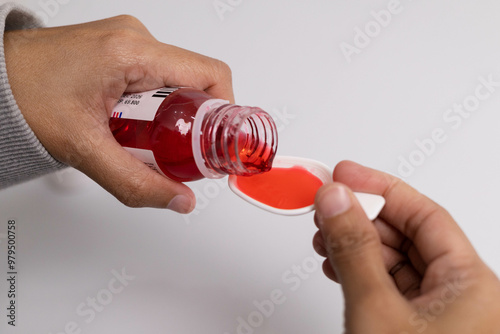 A close-up photo of someone pouring red cough syrup into a measuring spoon.