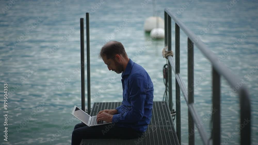 A person diligently working on their laptop while enjoying the serene beauty of the water nearby