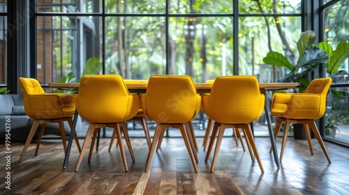 A modern office meeting room featuring vibrant yellow chairs around a wooden table, surrounded by large floor-to-ceiling windows with a lush green outdoor view