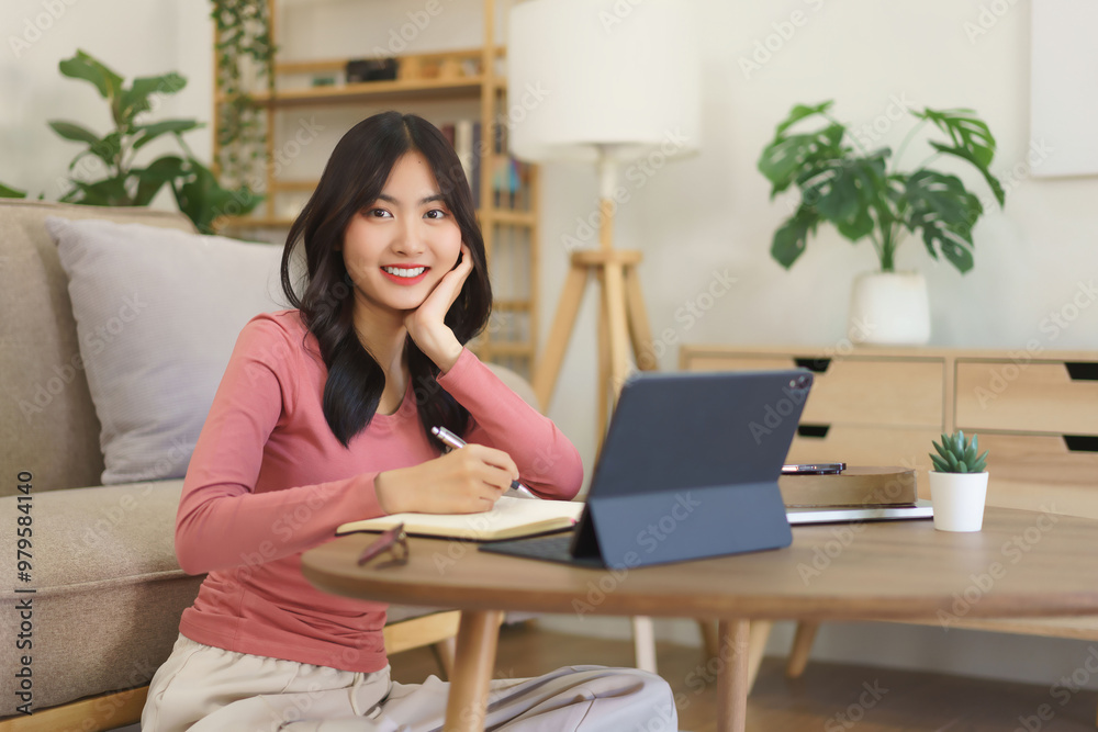 Young businesswoman reading business data on tablet and writing note in paper while working at home Young businesswoman reading business data on tablet and writing note in paper while working at home