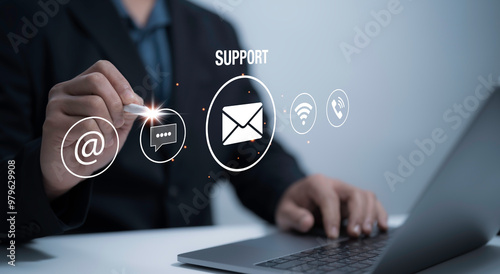 Support or connect with our customer support hotline. A businessman using a tablet touches the virtual screen with contact icons email, address, live chat and internet Wi-Fi