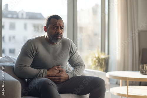 Man experiencing severe abdominal pain, pressing his hands to his stomach while sitting on a sofa