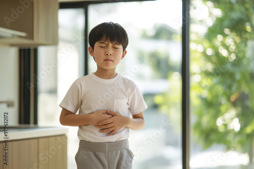Young boy is feeling unwell and holding his stomach, experiencing discomfort or pain in his abdomen Free Download Young boy is feeling unwell and holding his stomach, experiencing discomfort or pain in his abdomen - GFXLoad