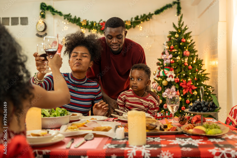 A joyful family gathers around the dinner table celebrating Christmas. The father, dressed in a Santa hat, gives a gift to the child, while everyone smiles with warmth and festive decorations. A joyful family gathers around the dinner table celebrating Christmas. The father, dressed in a Santa hat, gives a gift to the child, while everyone smiles with warmth and festive decorations.