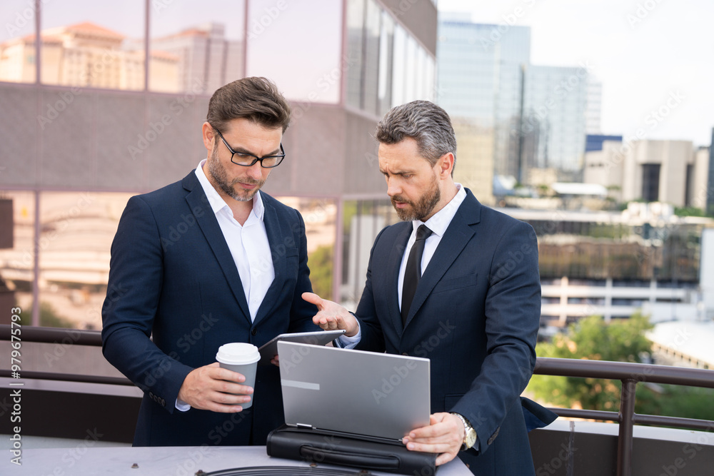 Two entrepreneurs near the office on the street. Business meeting of friends outdoors. Business mens with takeaway coffee and laptop outdoor. Business men team using laptop outdoor. Two businessman Two entrepreneurs near the office on the street. Business meeting of friends outdoors. Business mens with takeaway coffee and laptop outdoor. Business men team using laptop outdoor. Two businessman