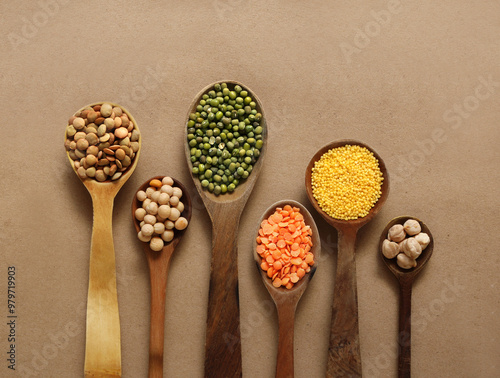 Wooden spoons with porridge, peas, dry millet groats, chickpeas, red lentil, mung beans on the brown background.