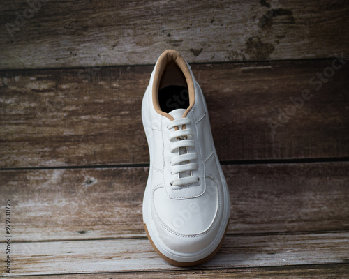 Elegant white eco-leather sneakers with brown sole detail, top view., on a wooden background