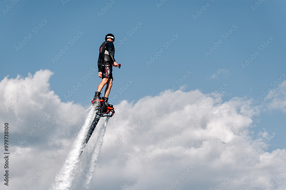 Athlete is flying using flyboard powerful water jet pack on the background of cloudy sky Athlete is flying using flyboard powerful water jet pack on the background of cloudy sky