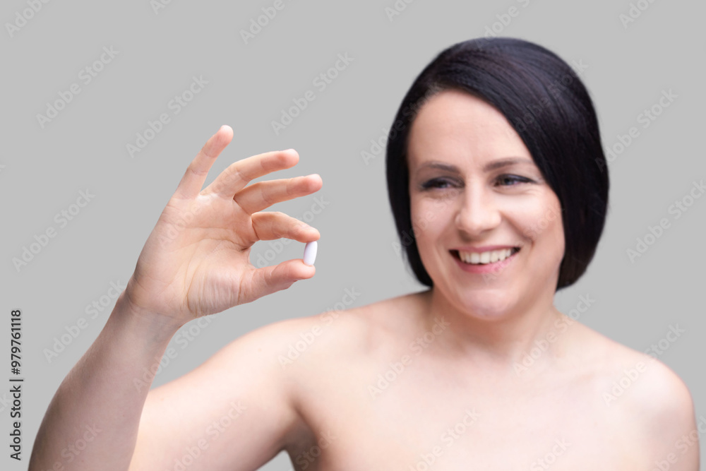 Woman holding a white pill in hand with a neutral background. Woman holding a white pill in hand with a neutral background.