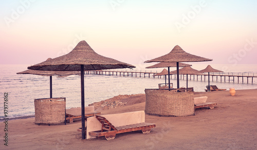 Empty beach with pier sun umbrella and loungers at purple sunset, color toning applied.