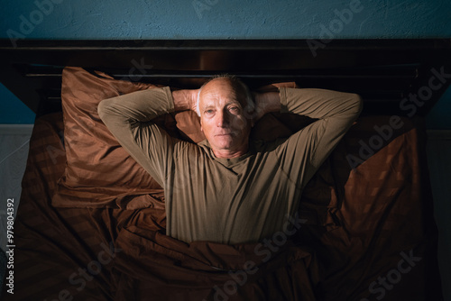 Old man can't sleep at night suffers from insomnia and bad thoughts late in the dark lying in the bedroom