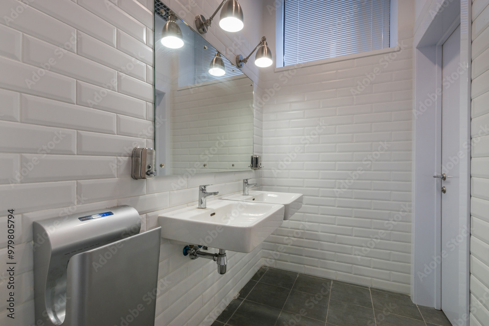 Fototapeta premium A public bathroom in an office corporate building. A mirror over the sinks and a hand .dryer.