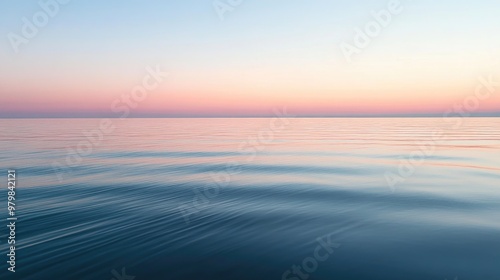 A calm, glassy ocean reflecting the pastel colors of the sky during sunrise, with small ripples in the water