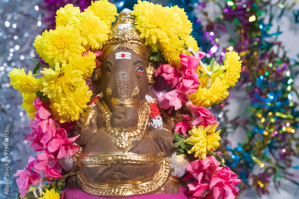 Hindu god Ganesha statue made of clay decorated with flower garlands on bokeh effect background. Closeup Hindu god Ganesha statue made of clay decorated with flower garlands on bokeh effect background. Closeup