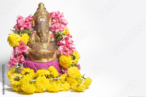 Ganesha statue made of clay decorated with flower garlands at home on Ganesha Chaturthi festival celebration on white background.