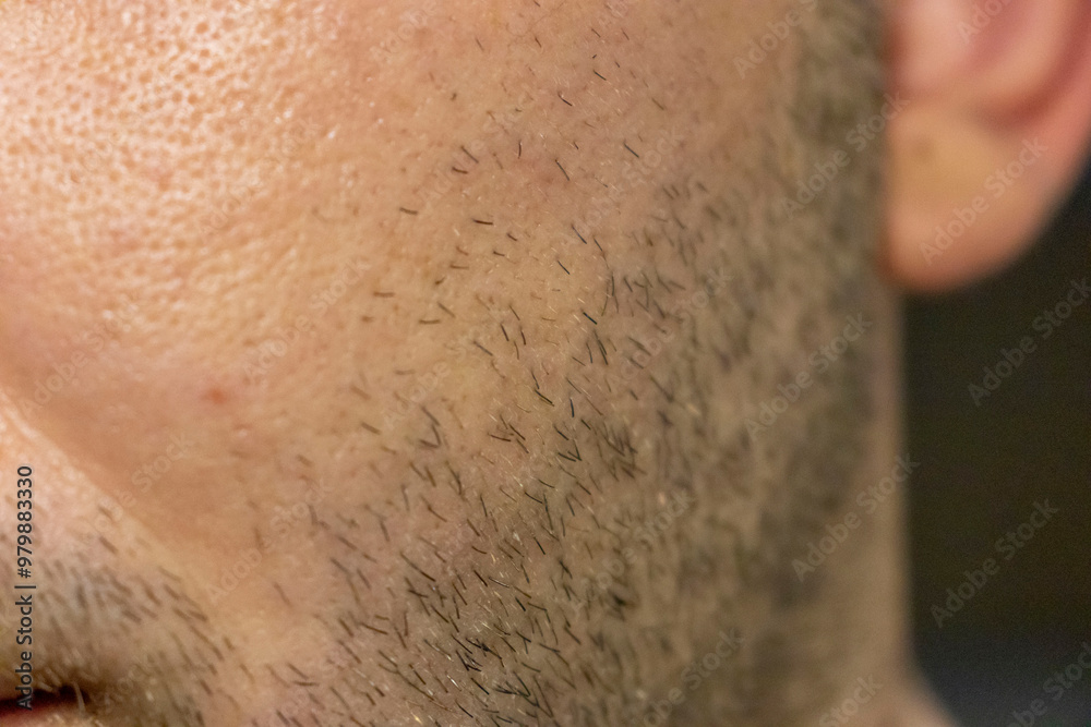 Naklejka premium Close-up of a man's cheek showing facial hair stubble and skin texture. The image highlights the details of hair follicles and skin pores.