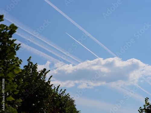 Airplane condensation trails (contrails) in the blue sky going out of a cloud