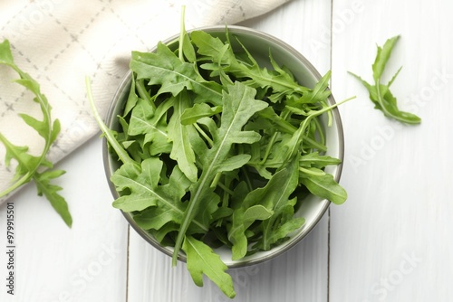 Fresh green arugula leaves in bowl on white wooden table, top view photo