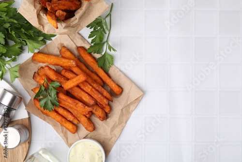 Sweet potato fries, parsley and sauce on white tiled table, top view. Space for text photo