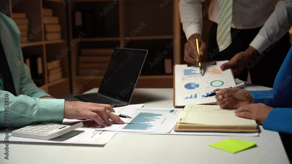 Strategic Insights: A team of business professionals analyzes financial data under the guidance of their leader, showcasing focused collaboration in a dimly lit office setting. Strategic Insights: A team of business professionals analyzes financial data under the guidance of their leader, showcasing focused collaboration in a dimly lit office setting.