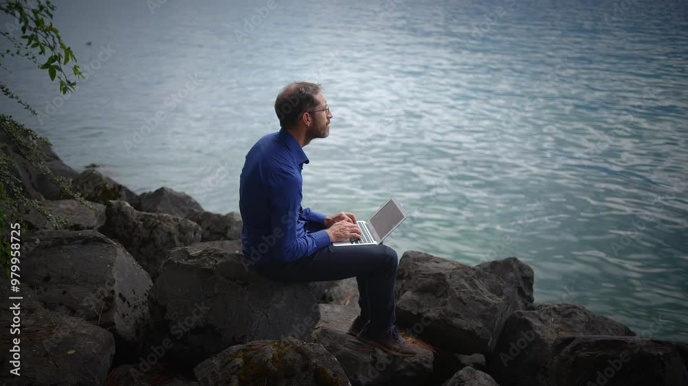 A man focused on his laptop at the waters edge, blending technology with tranquility A man focused on his laptop at the waters edge, blending technology with tranquility