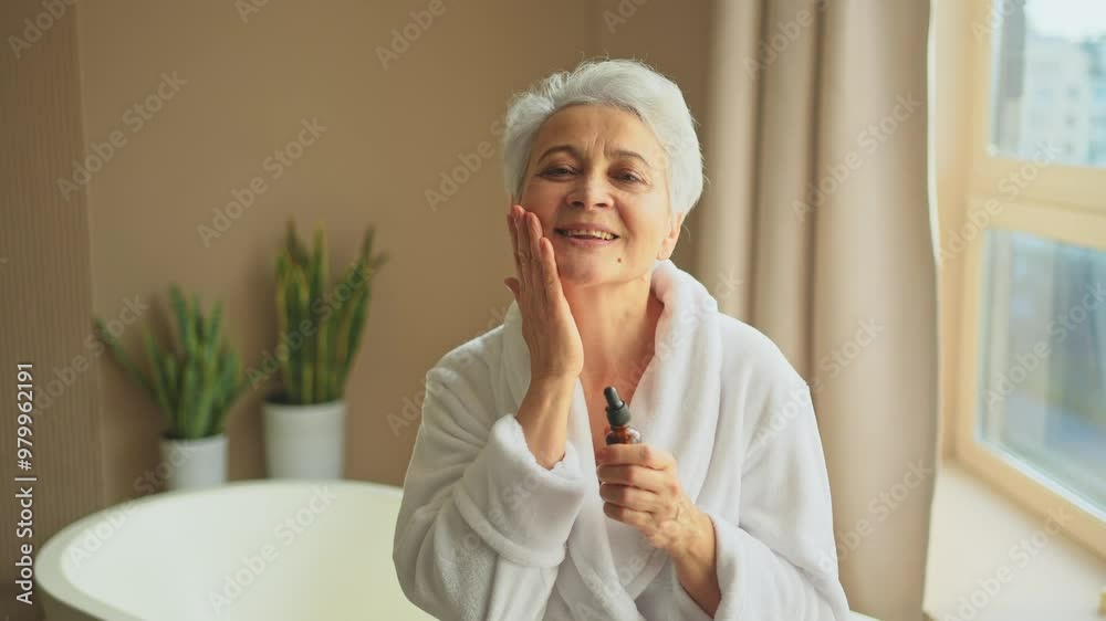 Woman applying natural drops cosmetics oil to face skin. Mature adult old woman applying nourishing anti age serum with pipette doing daily beauty routine. Senior woman gets kin scare facial treatment Woman applying natural drops cosmetics oil to face skin. Mature adult old woman applying nourishing anti age serum with pipette doing daily beauty routine. Senior woman gets kin scare facial treatment