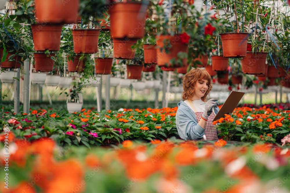 Young redhead botanist doing checklist in greenhouse full of flowers. Young redhead botanist doing checklist in greenhouse full of flowers.