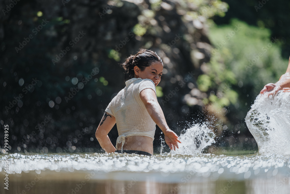 Fototapeta premium A happy woman joyfully splashes water in a beautiful natural setting, surrounded by lush greenery. The image captures the essence of fun, summer, and outdoor adventure.