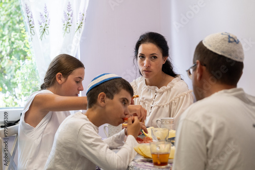 jewish family celebrating hanukkah, israel, boy in kippah, jewish holidays, yom kippur feast, table with food, honey, donuts, family holiday