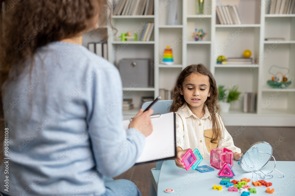 Cute little girl sitting at the table and having a training session with speech therapist Cute little girl sitting at the table and having a training session with speech therapist