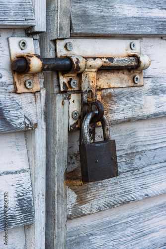 Rusty padlock and latch on white aged weathered closed wooden door. Closeup of rusted metal lock and old vintage rustic texture.  Shabby chic design. Security safety and industrial concept. Copy space photo