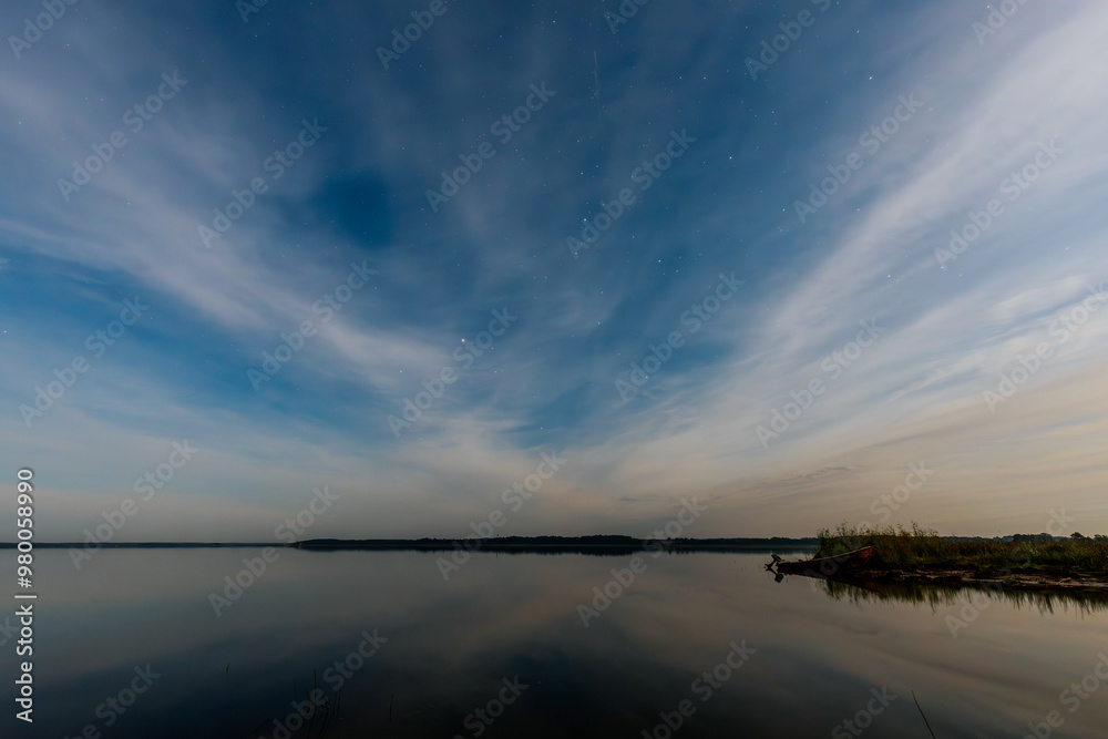 A tranquil lake at dusk, with small boats lined along the shore. The smooth water reflects the evening sky, filled with soft clouds and a few stars. The calm atmosphere creates a peaceful A tranquil lake at dusk, with small boats lined along the shore. The smooth water reflects the evening sky, filled with soft clouds and a few stars. The calm atmosphere creates a peaceful