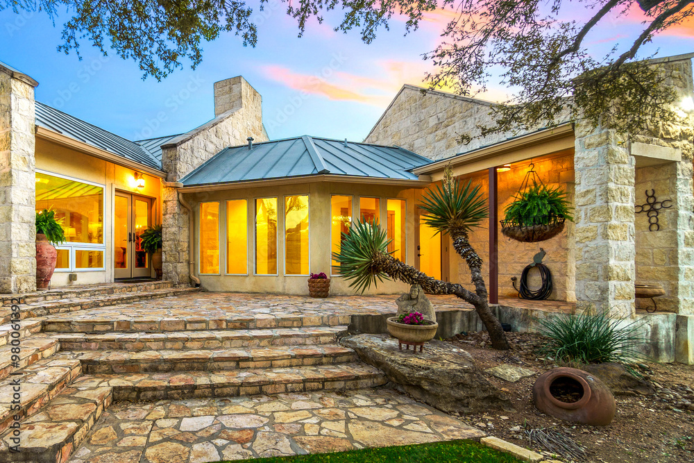 Obraz premium Stunning stone house with large windows and landscaped garden at sunset in a serene setting