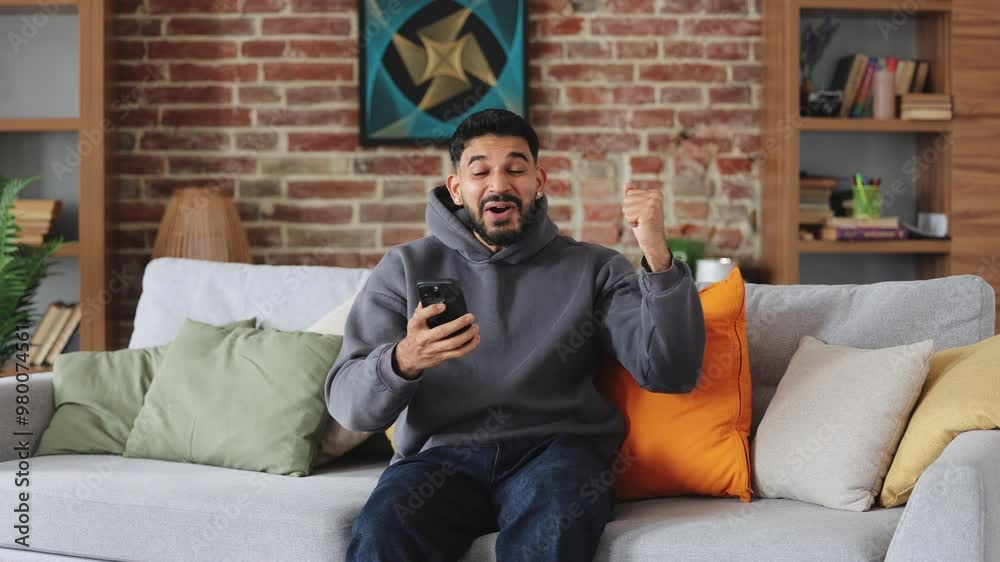 Expressive muslim man looking at cellular phone screen and saying wow while cheering for triumph of jackpot winning. Young gambler taking chance with bet and getting valuable prize on score. Expressive muslim man looking at cellular phone screen and saying wow while cheering for triumph of jackpot winning. Young gambler taking chance with bet and getting valuable prize on score.